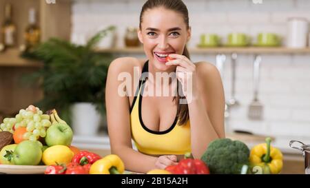 Donna sportiva mordente pomodoro ciliegia in casa cucina Foto Stock