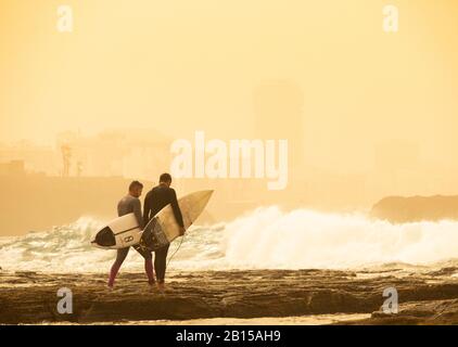 Las Palmas, Gran Canaria, Isole Canarie, Spagna. 23rd febbraio 2020. I surfisti che si dirigono verso l'esterno come una delle peggiori tempeste di polvere sahariane negli ultimi anni riducono la visibilità a 400 metri a Las Palmas, E ha causato la cancellazione di più di 200 flighs il sabato come polvere e sabbia che soffiano su forti venti dalle coperte del Sahara Gran Canaria così come altre isole Canarie. Credito: Alan Dawson/Alamy Live News Foto Stock