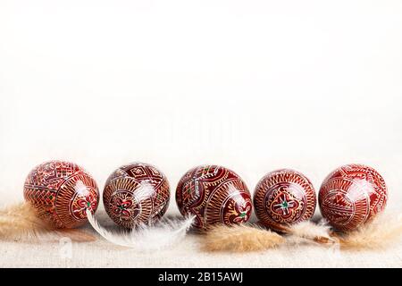 Tradizionale ucraino Pysanka messo in linea con le piume su sfondo bianco. Uova di Pasqua decorate, tradizionali per la cultura dell'Europa orientale. Copia sp Foto Stock