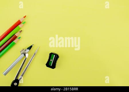 Studiare i materiali che contengono quattro pastelli di matita colorati diversi, una matita attaccata ad una bussola della matita e un affilatore della matita nero sparso su un yel Foto Stock