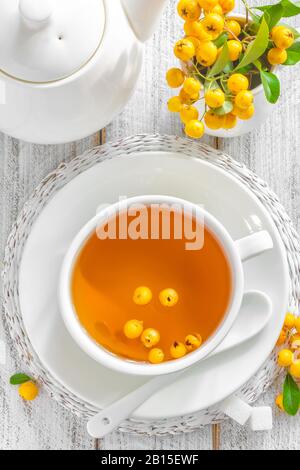 Tè di biancospino in una tazza con frutti di bosco freschi su tavola di legno bianco, sano erbe di guarigione bevanda calda Foto Stock