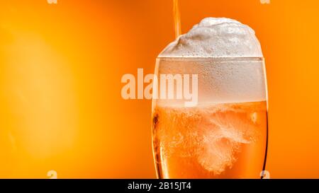 La birra lager si deposita nel bicchiere con un tappo bianco di schiuma Foto Stock