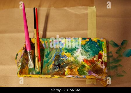 Vernici a olio e pennelli per artisti in una tavolozza di miscelazione. Vernici a olio miste di colori e saturazione diversi. Diverse attrezzature per il disegno dei bambini, il disegno degli adulti e le scuole d'arte Foto Stock