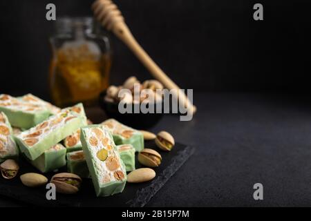 Torrone di organico a base di miele, pistacchi, nocciole, mandorle e i dadi su un rustico sfondo scuro. Foto Stock