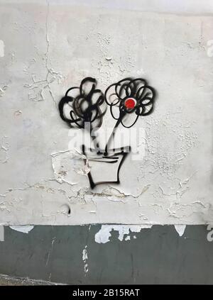 Due fiori neri con cerchio rosso al centro dipinto sulla parete bianca fessurata con bordo grigio, graffiti. Foto Stock