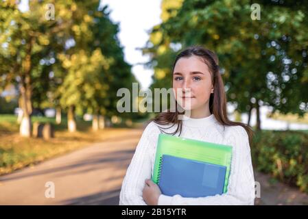 Ragazza scuola estate parco, mani notebook libri di testo e libri. Sfondo strada alberi erba verde. Spazio libero per il testo concetto di studiare scuola Foto Stock