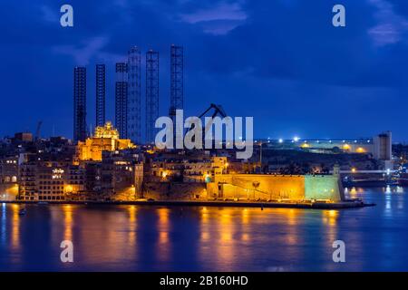 Città skyline di Senglea (L-Isla, Civitas Invicta) a Malta di notte, vista mare con gru cantiere sullo sfondo. Foto Stock