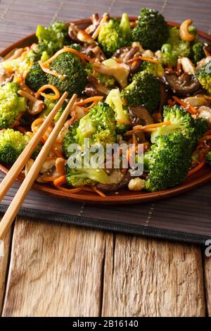 Mescolare fritti funghi shiitake, broccoli, carote e cashews vicino in un piatto sul tavolo. Verticale Foto Stock