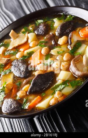 Zuppa di ceci vegetariana con verdure e funghi si avvicina in una ciotola sul tavolo. Verticale Foto Stock