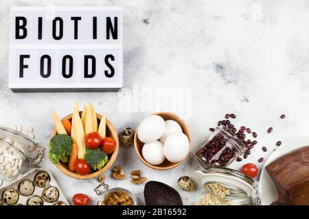 Cibo ricco di biotina. Cibo : uova di pomodoro noci fagioli mais avocado broccoli carota fegato farina d'avena su sfondo blu con scatola chiara iscrizione biotina Foto Stock