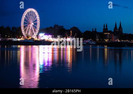 Ruota panoramica ed edifici sulla riva accanto al fiume Mosel a Coblenza, Germania. Luci che si riflettono nell'acqua. Foto Stock