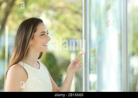 Profilo di una donna felice che controlla il tavolo del tempo in piedi alla fermata dell'autobus Foto Stock