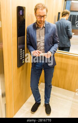 Un uomo d'affari moderno che utilizza un tablet digitale in ascensore. Foto Stock