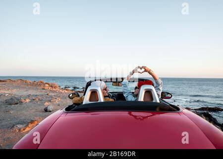 Coppia guida auto convertibile, viaggiando vicino all'oceano al tramonto, vista dal retro. Buone vacanze e viaggi in auto Foto Stock