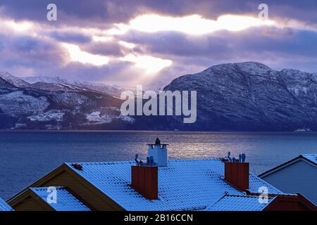 Vista panoramica sul villaggio di Ålvik, Hardanger, Hordaland, Norvegia. Bellissimo paesaggio invernale norvegese con tetto innevato, camini, fiordo e mouta Foto Stock