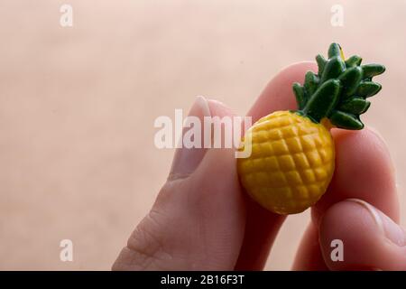 Mano che tiene un piccolo ananas miniatura su uno sfondo sul display Foto Stock