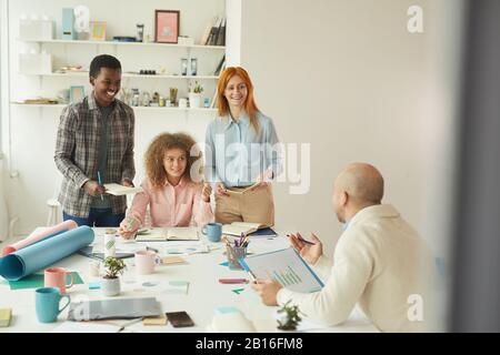 Ritratto di diversi team di business che collaborano al progetto aziendale durante la riunione in moderno ufficio bianco e sorridente allegramente Foto Stock