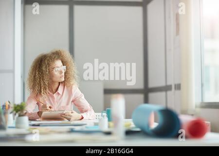 Ritratto di funky giovane donna d'affari indossando occhiali guardando la finestra mentre daydreaming sul posto di lavoro, copia spazio Foto Stock