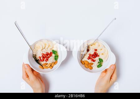 Mani di donna che tengono due ciotole di farina d'avena sana di colazione con frutta e noci, piatto lay. Foto Stock