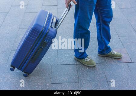 Un uomo con una valigia blu su ruote in attesa di trasporto. Foto Stock