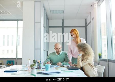 Gruppo di tre persone aziendali che discutono di documenti mentre lavorano al tavolo in ufficio, copia spazio Foto Stock