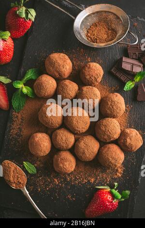 Tartufi Di Cioccolato Fondente Fatti In Casa Rivestiti In Polvere Di Cacao Su Sfondo Ardesia Nera. Gustosi Dolci Al Cioccolato Fatti In Casa Foto Stock