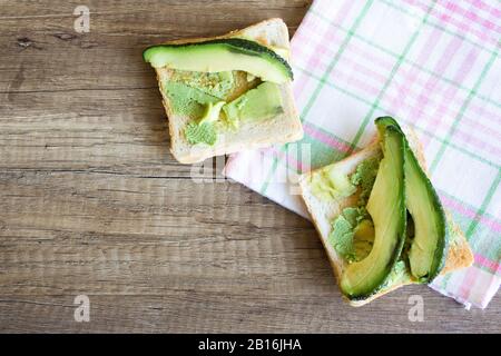 Toast con avocado su un tavolo in legno, vista dall'alto. Concetto di alimentazione sana Foto Stock