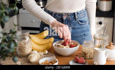 Aggiungere frutta alla colazione farinata d'avena porridge ciotola. Donna che prepara una sana colazione in cucina. Concetto di sano mangiare e stile di vita Foto Stock