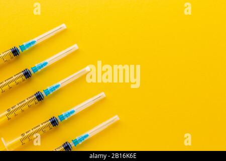 Siringhe monouso su sfondo giallo brillante. Vaccinazione contro l'influenza e il coronavirus. Concetto di assistenza sanitaria. Iniezione medica. Ago, dosaggio Foto Stock
