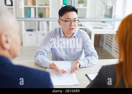 Ritratto di giovane asiatico che risponde alle domande durante l'intervista di lavoro seduta attraverso due HR manager, copia spazio Foto Stock