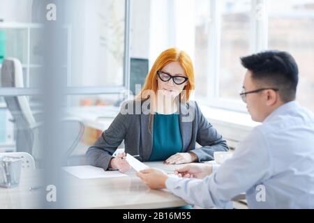 Ritratto del manager HR con capelli rossi intervistando il giovane uomo per la posizione di lavoro in ufficio, copia spazio Foto Stock