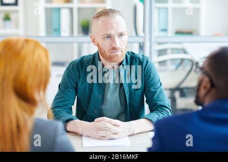 Ritratto di uomo contemporaneo adulto che ascolta i responsabili di HR durante l'intervista di lavoro in ufficio, copia spazio Foto Stock