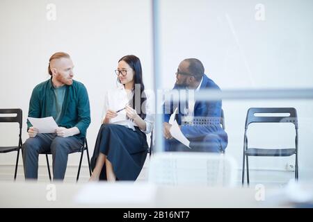 Gruppo multietnico di persone in attesa in linea per colloqui di lavoro e chiacchierare dietro muro di vetro , copia spazio Foto Stock