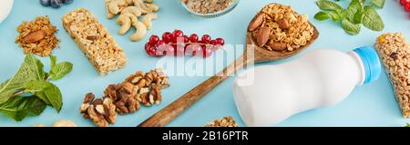 Composizione alimentare di frutta secca, bottiglia di yogurt, frutti di bosco, barrette di cereali e menta su sfondo blu, colpo panoramico Foto Stock