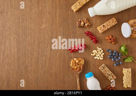 Vista dall'alto di frutti di bosco, noci, barrette di cereali e bottiglie di yogurt e latte su sfondo di legno Foto Stock