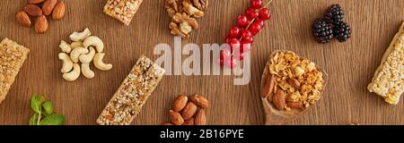 Vista dall'alto della composizione alimentare di frutti di bosco, noci e barrette di cereali su sfondo di legno, colpo panoramico Foto Stock