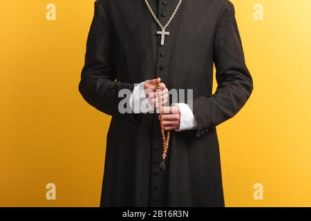 vista ritagliata del sacerdote cattolico con perline di rosario in legno isolato su giallo Foto Stock