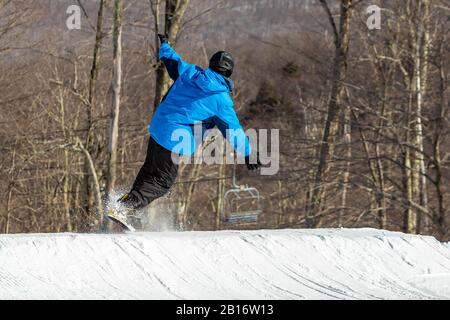Snowboarder divertirsi saltando in stazione sciistica in aria dal retro Foto Stock
