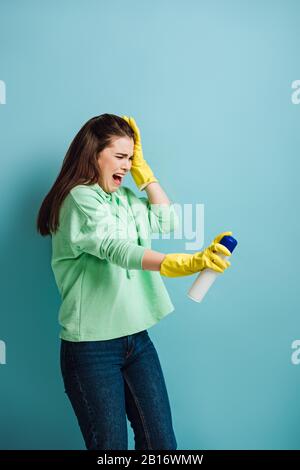 la casalinga disafflionata imgracing e la testa toccante mentre spruzza il deodorante d'aria su sfondo blu Foto Stock