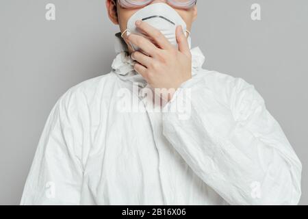 vista ritagliata dell'epidemiologo in tuta hazmat con maschera respiratore a contatto isolato su grigio Foto Stock