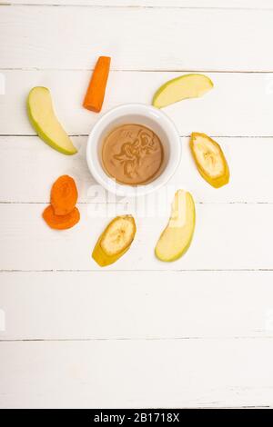 Vista dall'alto del cibo per bambini in una ciotola con frutta a fette e carota su una superficie di legno bianco Foto Stock