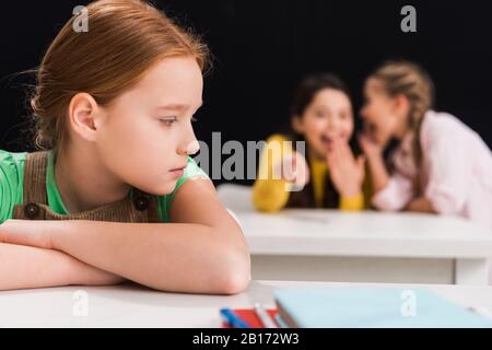 fuoco selettivo di scolari rovesciati seduti vicino a compagni di classe ridendo e pettegolezzi in classe isolato su nero, concetto di bullismo Foto Stock