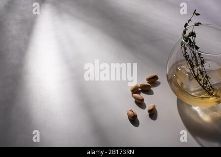 vetro trasparente con erba, cubetto di ghiaccio e whisky su tavolo bianco con ombra vicino al pistacchio Foto Stock