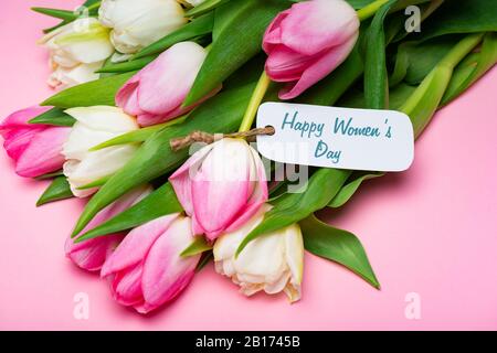 Bouquet di tulipani e etichetta di carta con scritta Happy Womens day su superficie rosa Foto Stock