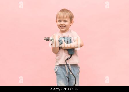 Felice ragazzo si alza e tiene un vero trapano elettrico di colore blu. Per gli articoli su apparecchi e attrezzi, la loro facilità d'uso e l'educazione dei bambini. Foto Stock