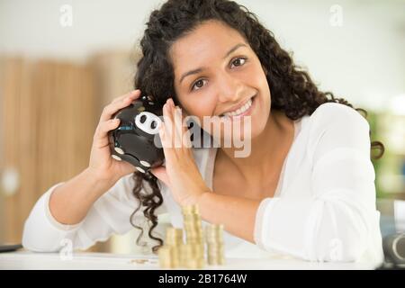 donna che scuote la banca piggy con espressione speranzosa Foto Stock