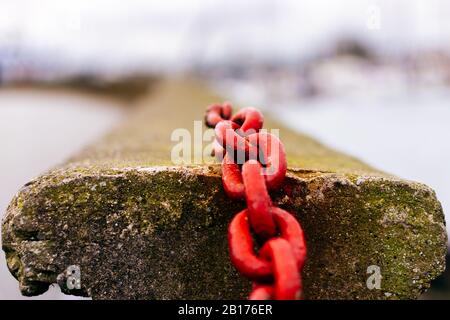 Primo piano di vecchia catena arrugginita rossa collegata a parete di cemento con sfondo sfocato Foto Stock