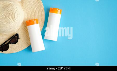 Crema solare o crema solare bottiglie senza etichette su sfondo blu con cappello da spiaggia e occhiali da sole. Disposizione piatta, vista dall'alto. Make-up estivo e cura della pelle Foto Stock