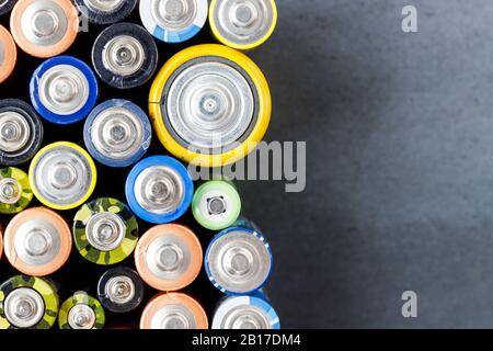 Primo piano delle estremità positive delle batterie colorate scaricate di diverse dimensioni e formati, vista dall'alto, spazio di copia. Batteria alcalina usata su retro nero Foto Stock