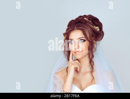 Bride pensare. Closeup ritratto testa shot felice gara mista daydreaming sorridente cute sicuro ragazza sposa donna isolato luce blu sfondo Foto Stock